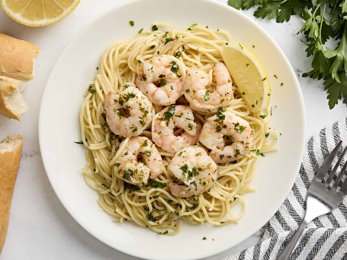 Overhead view of shrimp scampi on a bed of spaghetti on a plate.