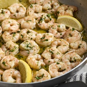 Close up of shrimp scampi in a skillet with lemon wedges.