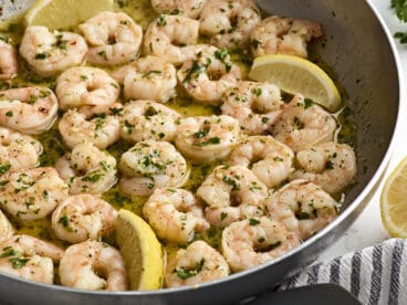 Close up of shrimp scampi in a skillet with lemon wedges.