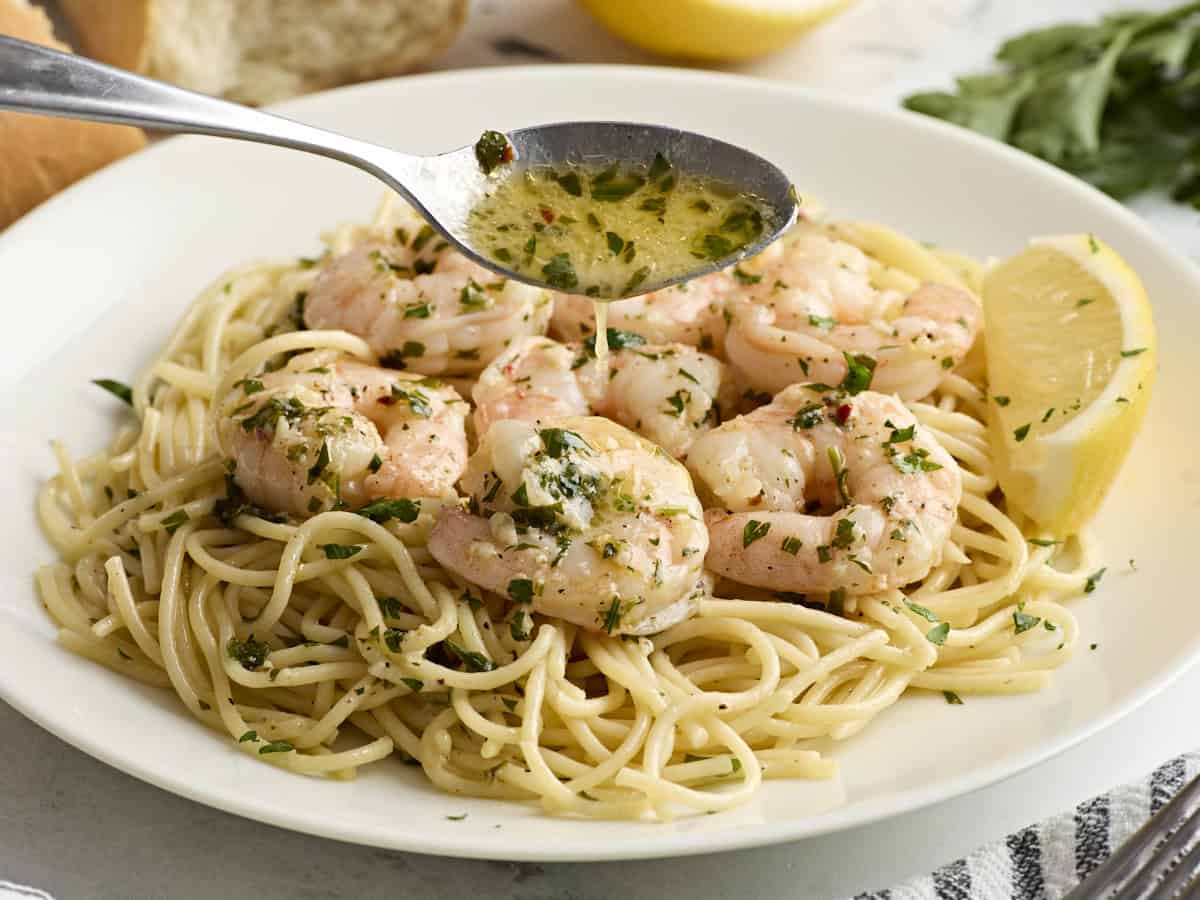 A spoon pouring garlic butter sauce over shrimp scampi and spaghetti.