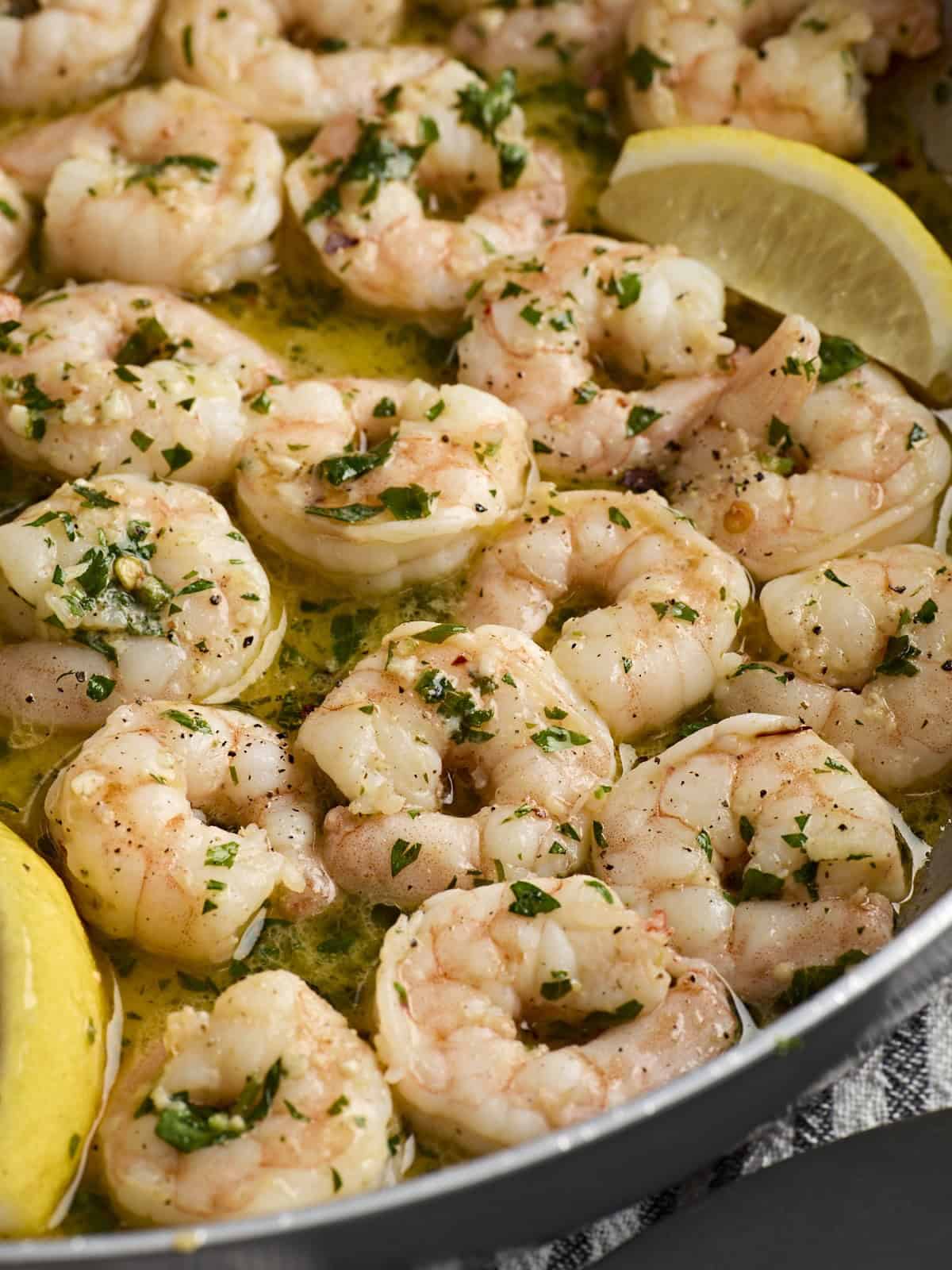 Close up of shrimp scampi in a skillet with lemon wedges.