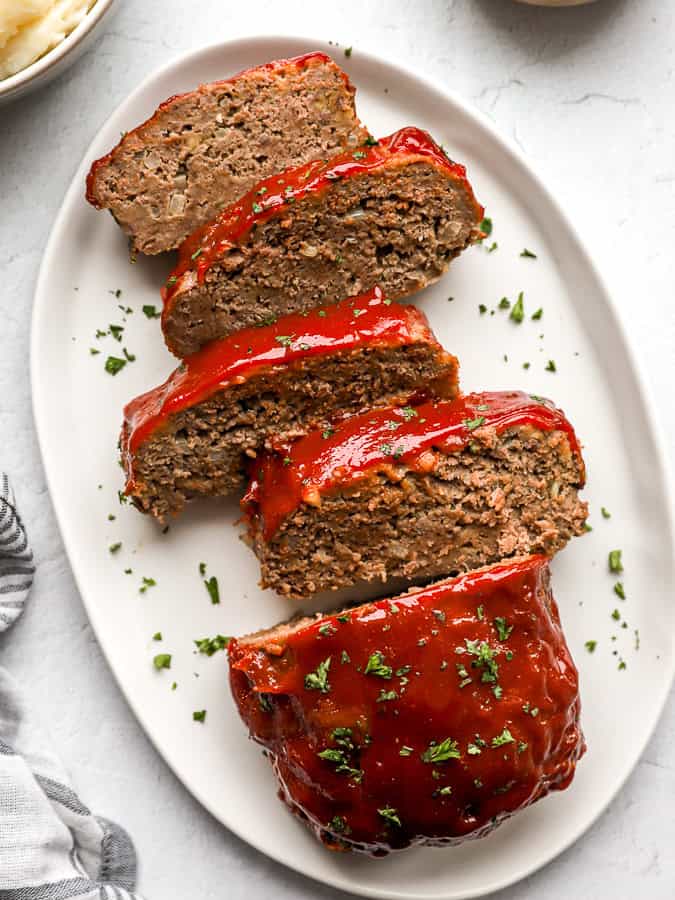 Overhead view of slices of homemade meatloaf, topped with a tomato glaze on a white platter.