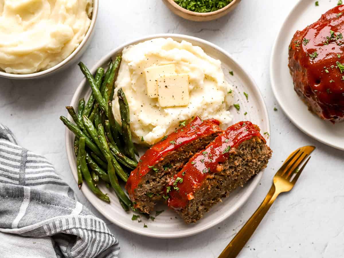 Overhead view of two meatloaf slices on a plate with mashed potatoes and green beans.