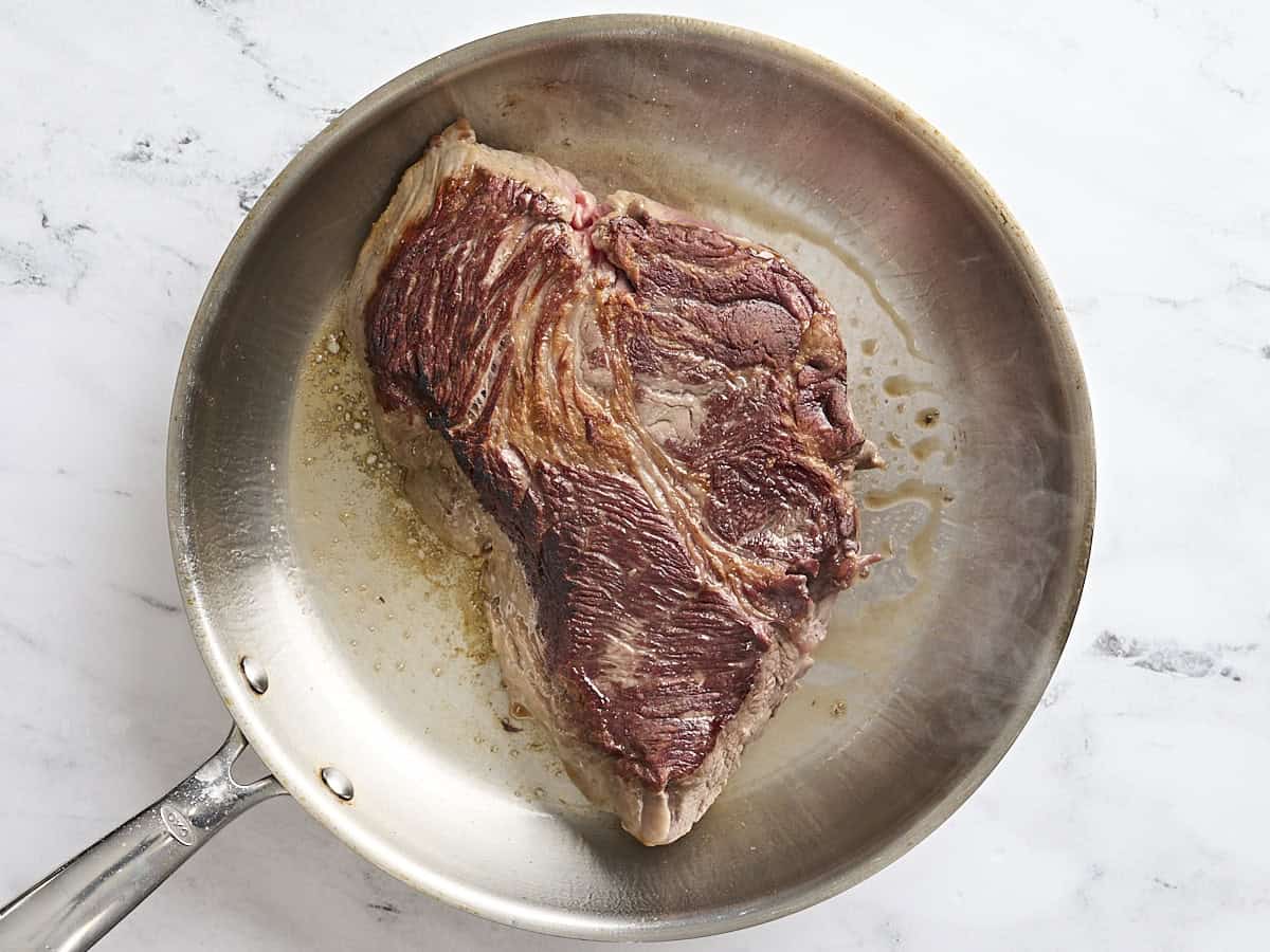 A chuck roast sauteing in a skillet.