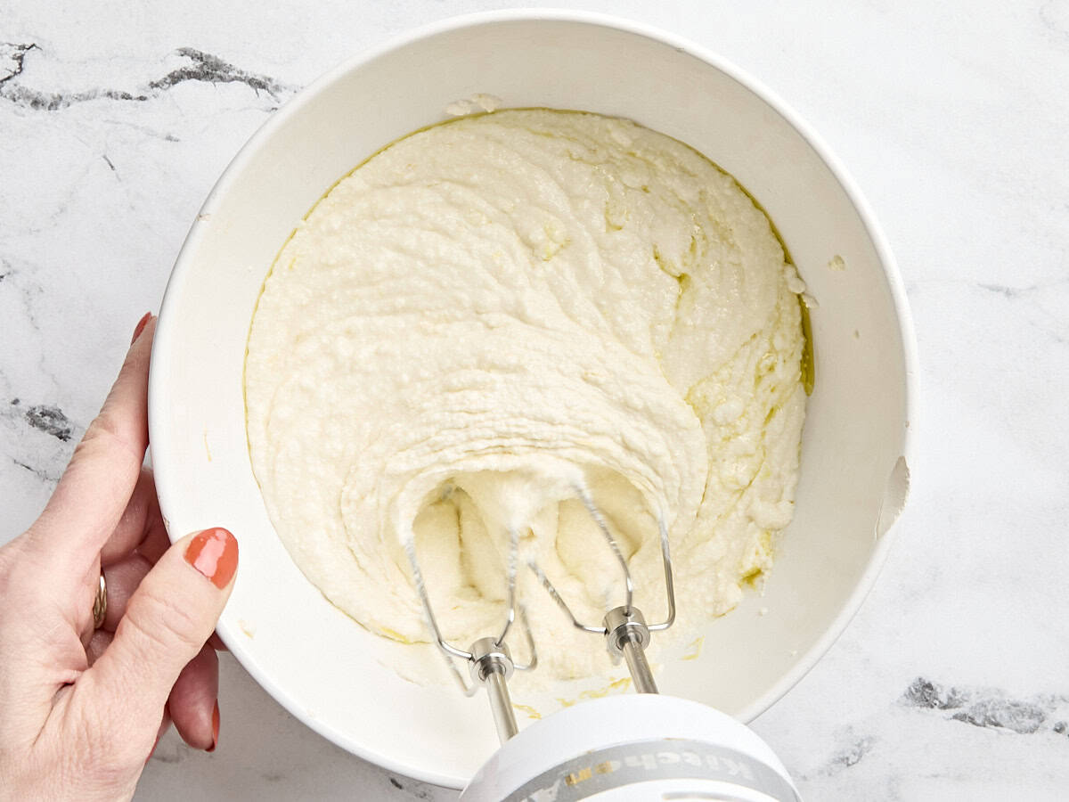 A hand mixer whipping ricotta in a mixing bowl.