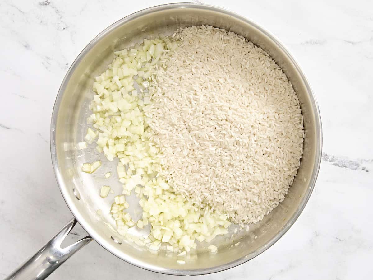 Uncooked white rice added to skillet with minced yellow onion.