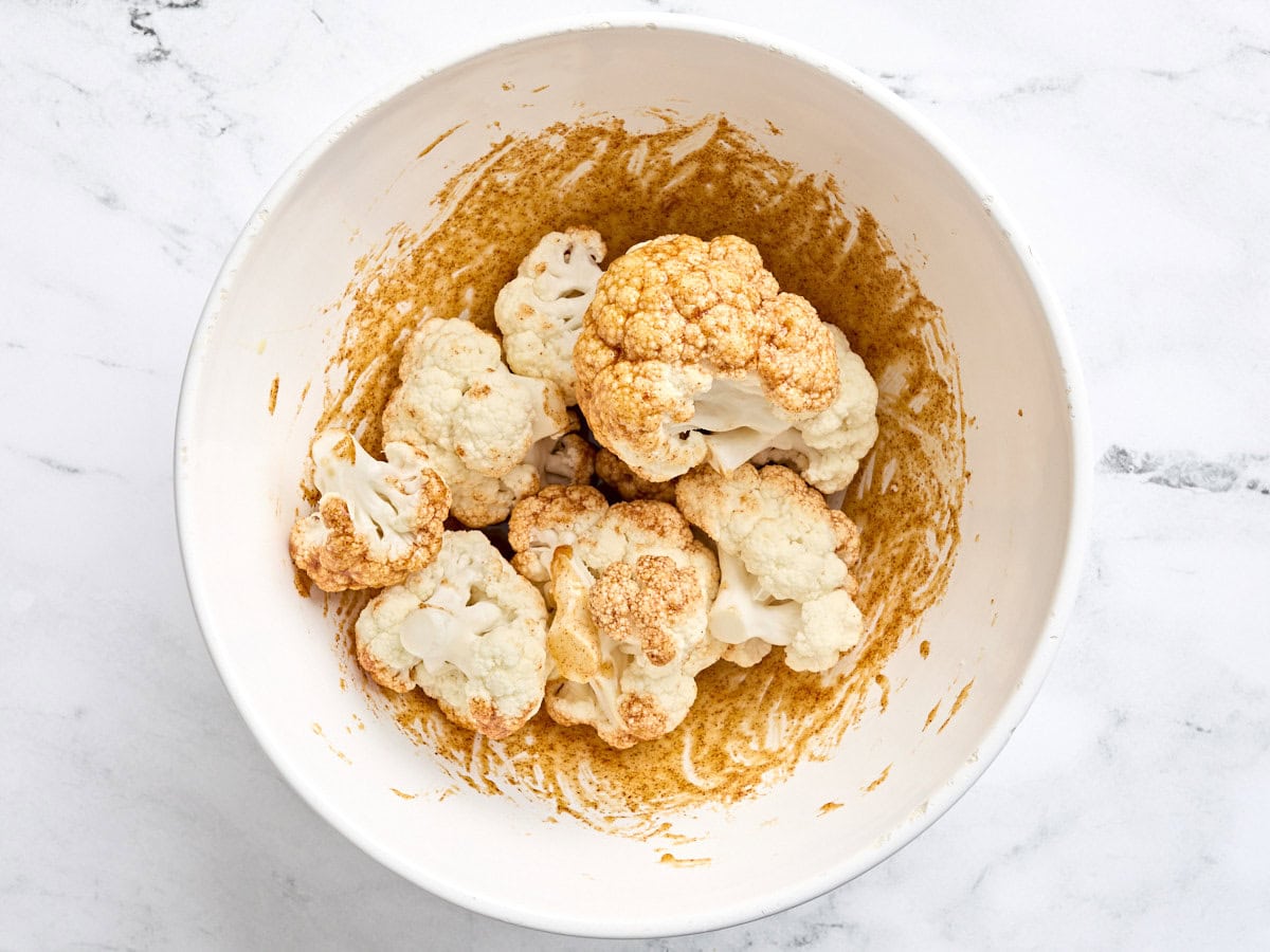 Cauliflower florets coated in a seasoning mix in a bowl.