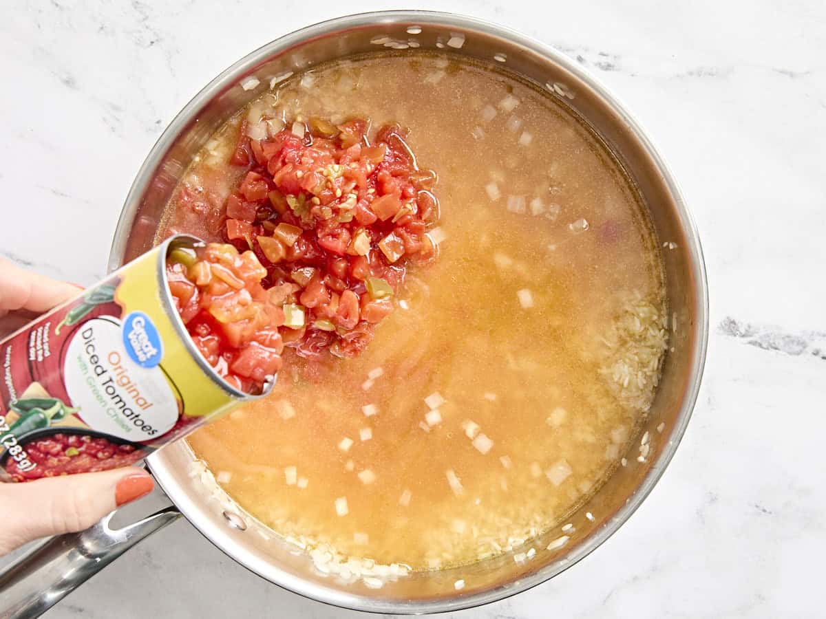 Vegetable broth and canned tomatoes with green chilis added to a skillet with onion and white rice to make spanish rice.