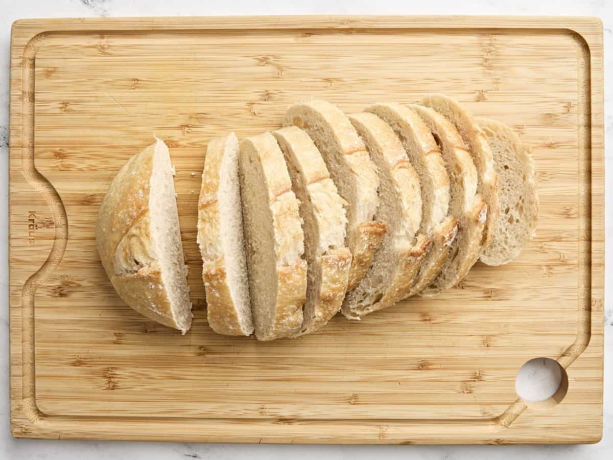 A loaf of sourdough bread cut into slices on a wooden cutting board.