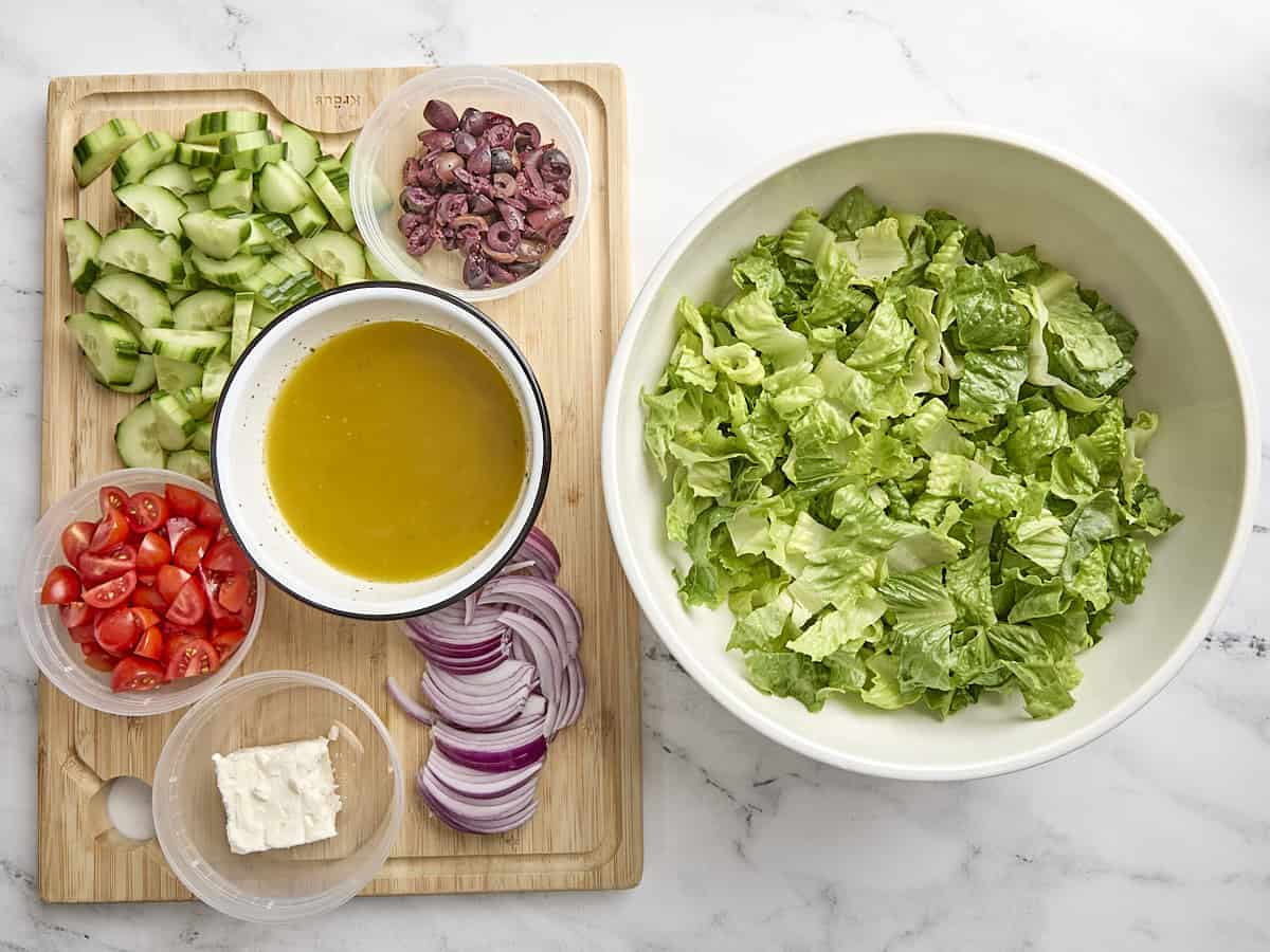 Over head view of greek salad ingredients on a wooden cutting board.