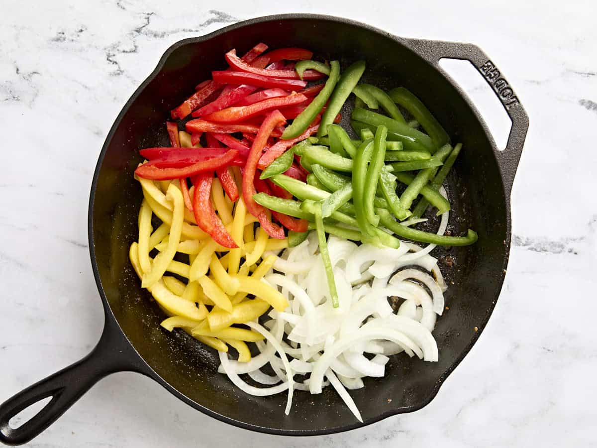 Sliced bell peppers and onion added to a skillet.