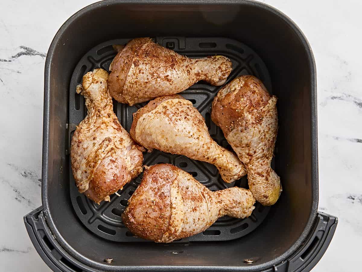 Seasoned chicken drumsticks arranged in an air fryer basket.