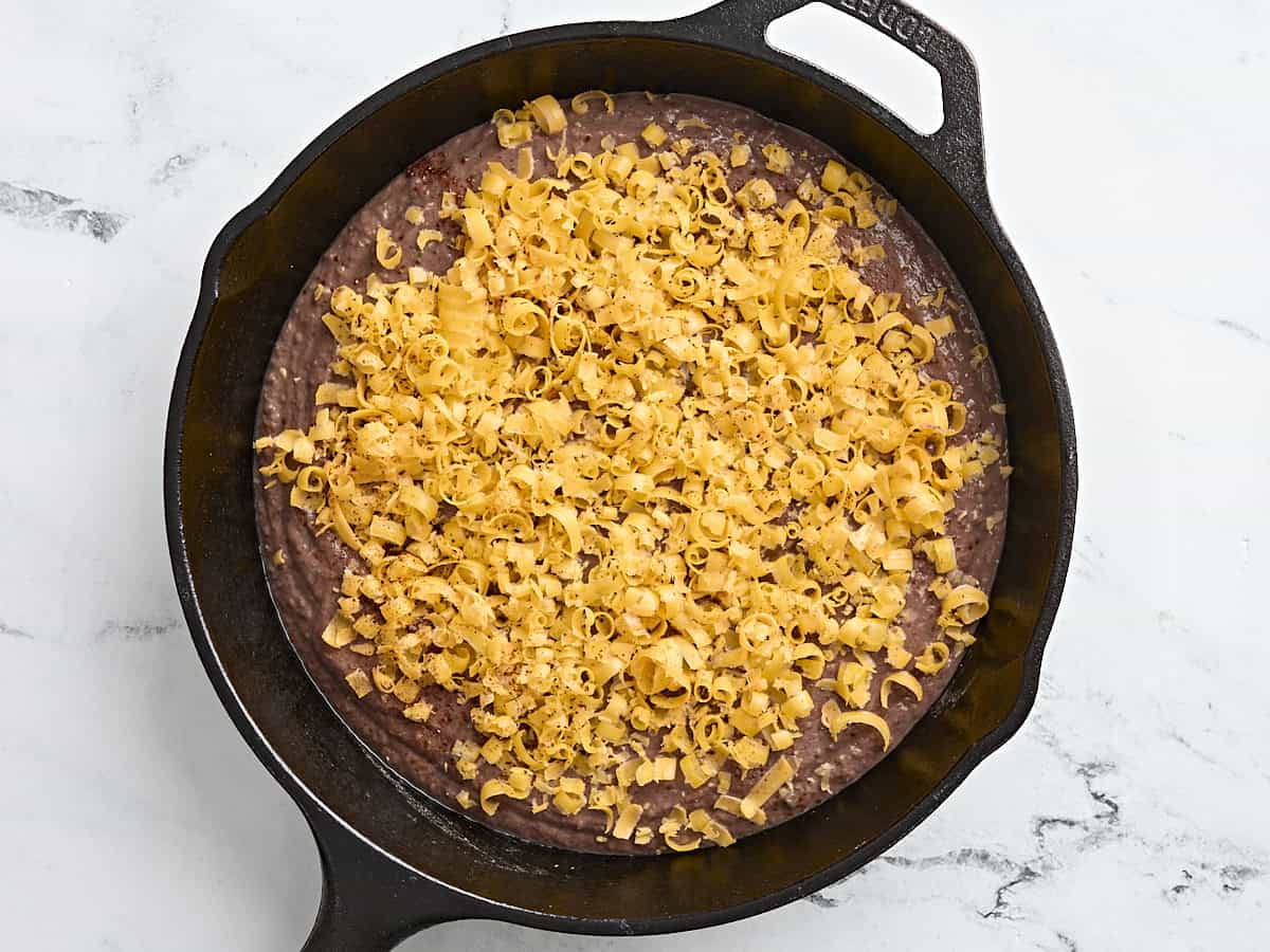 Black bean dip in a cast iron, topped with shredded cheese.