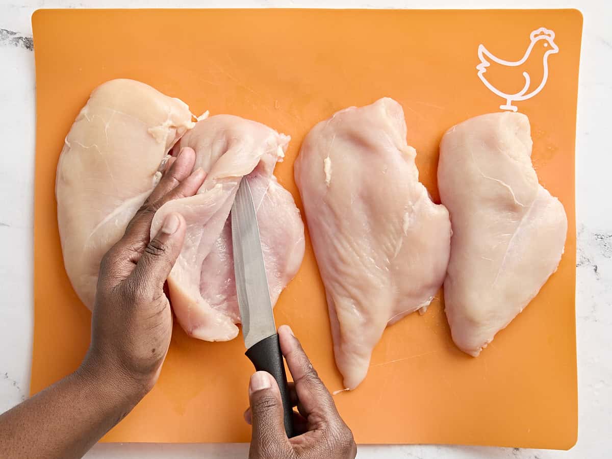 Chicken breasts on a meat preparation mat, with a knife slicing one for stuffing.