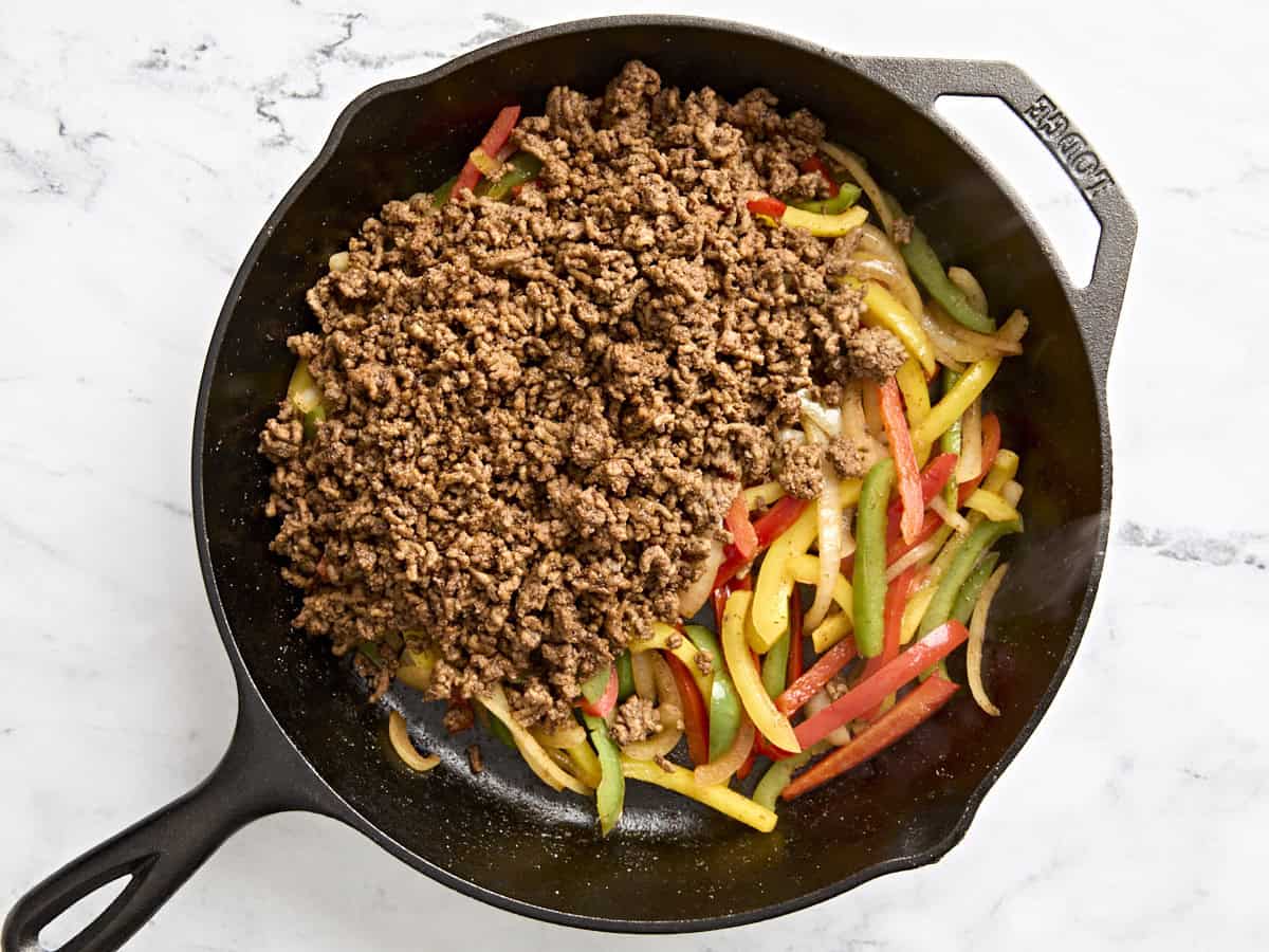 Sliced peppers added to browned ground beef in a skillet.