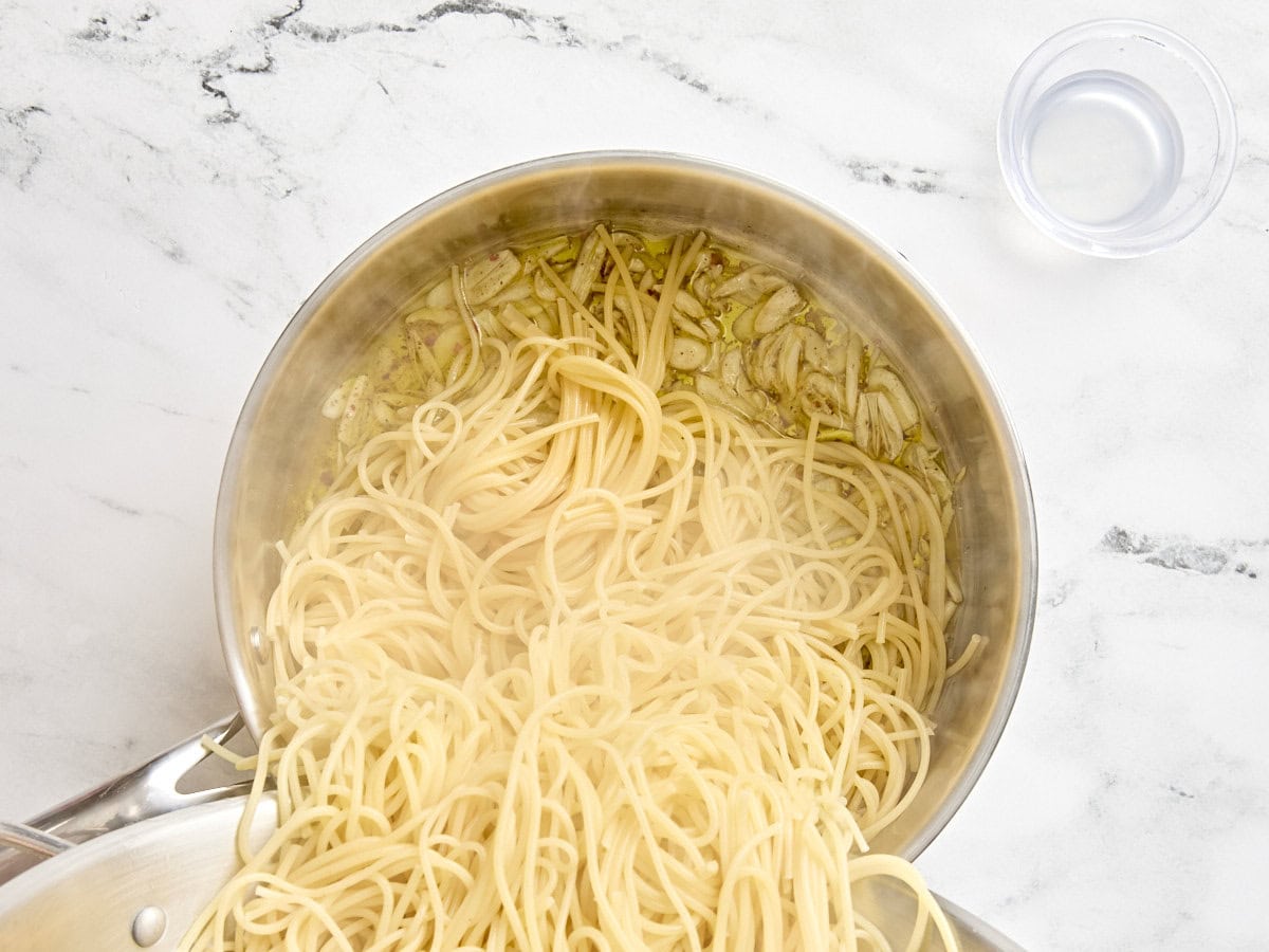 Spaghetti being poured into a saucepan.