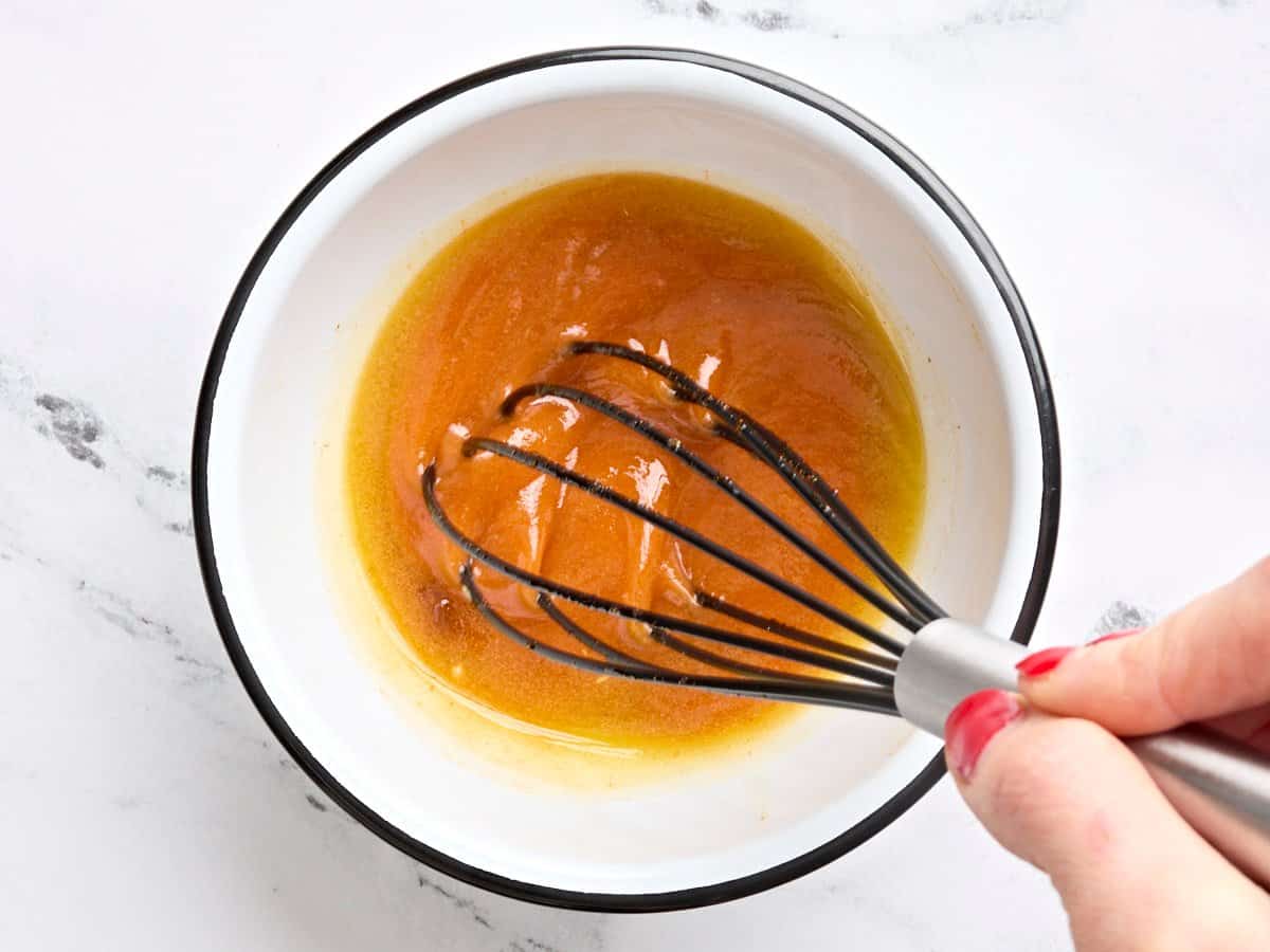 Melted butter being whisked into buffalo sauce in a bowl.