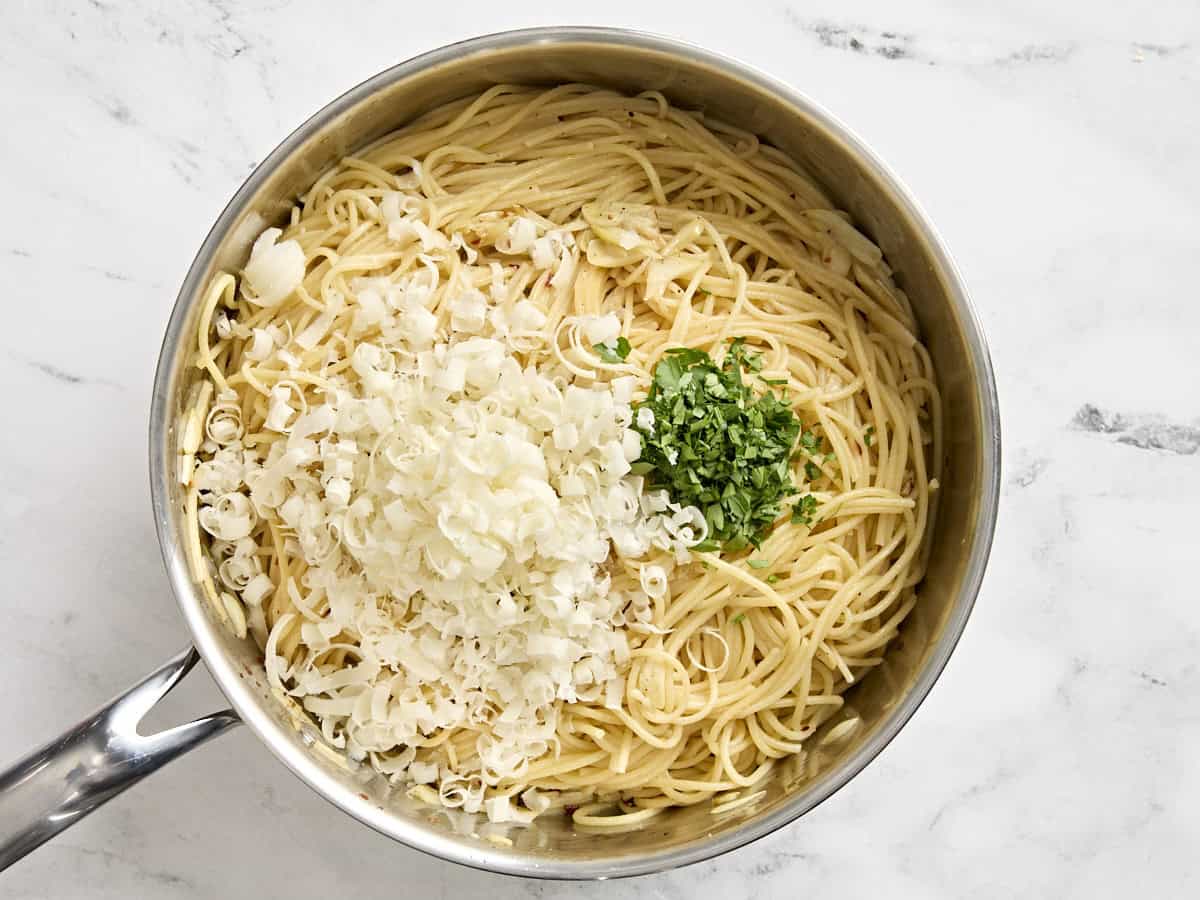 Parmesan cheese and fresh parsley added to spaghetti in a saucepan.