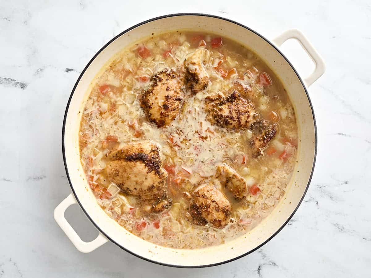 Greek chicken added to a skillet with orzo and diced vegetables.