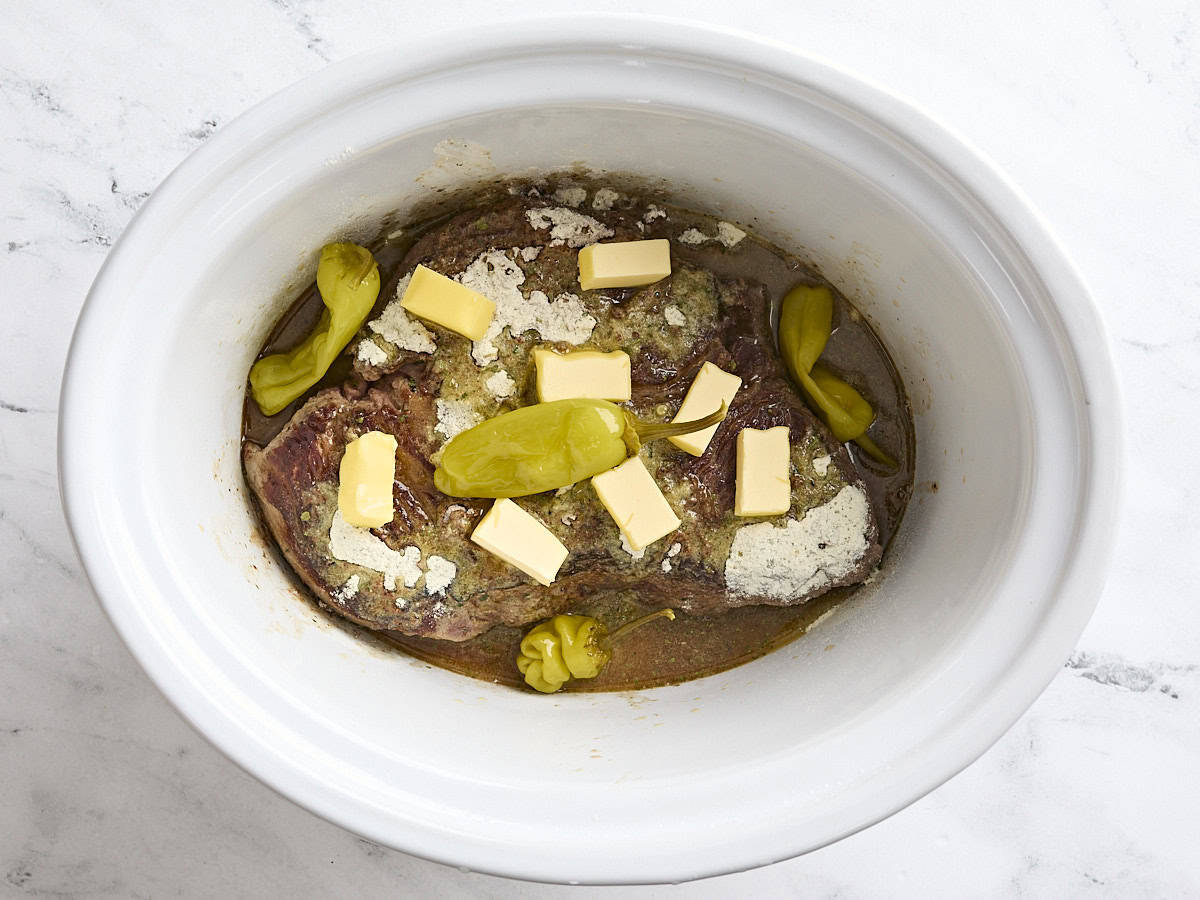 Cubed butter and pepperoncini added to a crockpot with chuck roast.