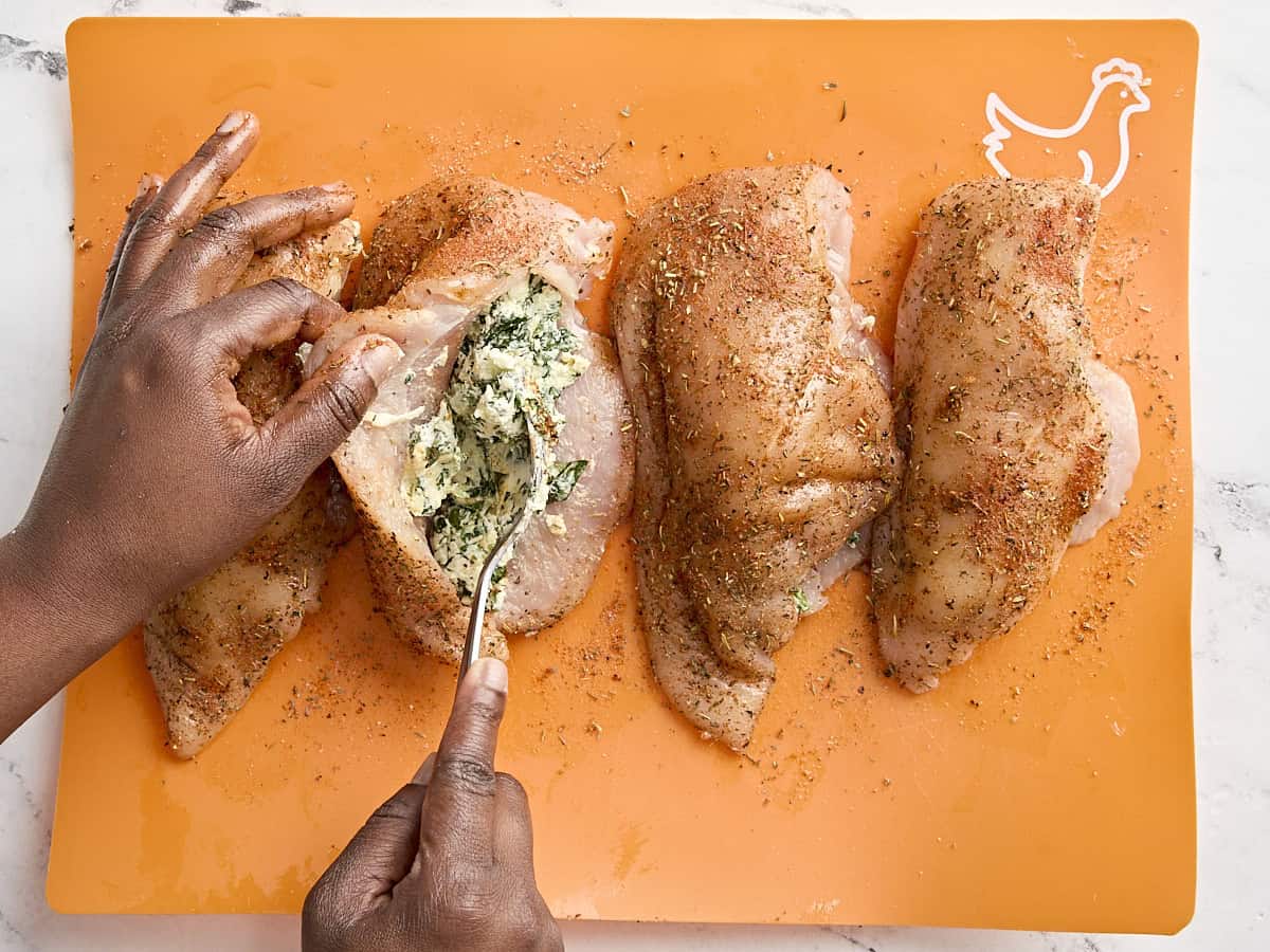 A hand stuffing chicken breasts with spinach stuffing.