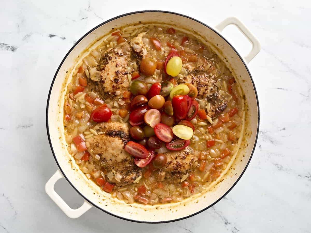 Slice grape tomatoes added to a skillet of Greek chicken and orzo.