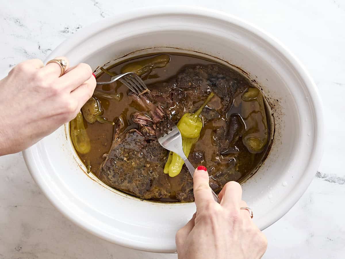 Two forks pulling the meat for Mississippi pot roast apart in a crockpot.