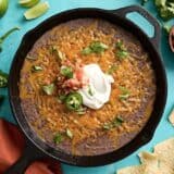 Overhead view of black bean dip in a cast iron skillet with sour cream and jalapenos on top.