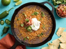 Overhead view of black bean dip in a cast iron skillet with sour cream and jalapenos on top.