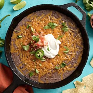 Overhead view of black bean dip in a cast iron skillet with sour cream and jalapenos on top.