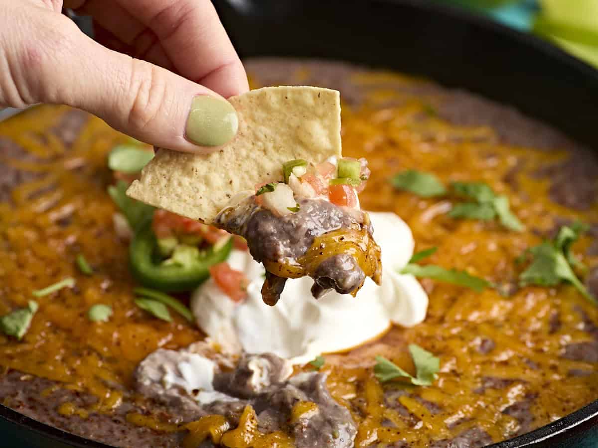 A tortilla chip dipped into black bean dip in a cast iron skillet.