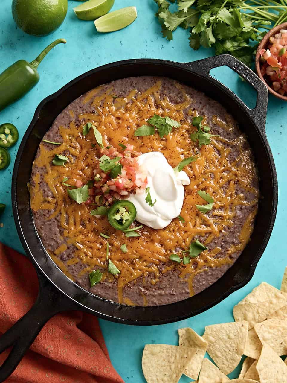 Overhead view of black bean dip in a cast iron skillet with sour cream and jalapenos on top.