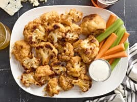 Overhead view of buffalo cauliflower wings on a plate with celery sticks, carrot sticks, and dip.