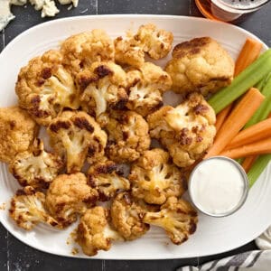 Overhead view of buffalo cauliflower wings on a plate with celery sticks, carrot sticks, and dip.