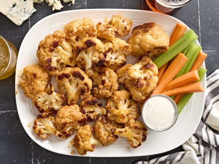 Overhead view of buffalo cauliflower wings on a plate with celery sticks, carrot sticks, and dip.