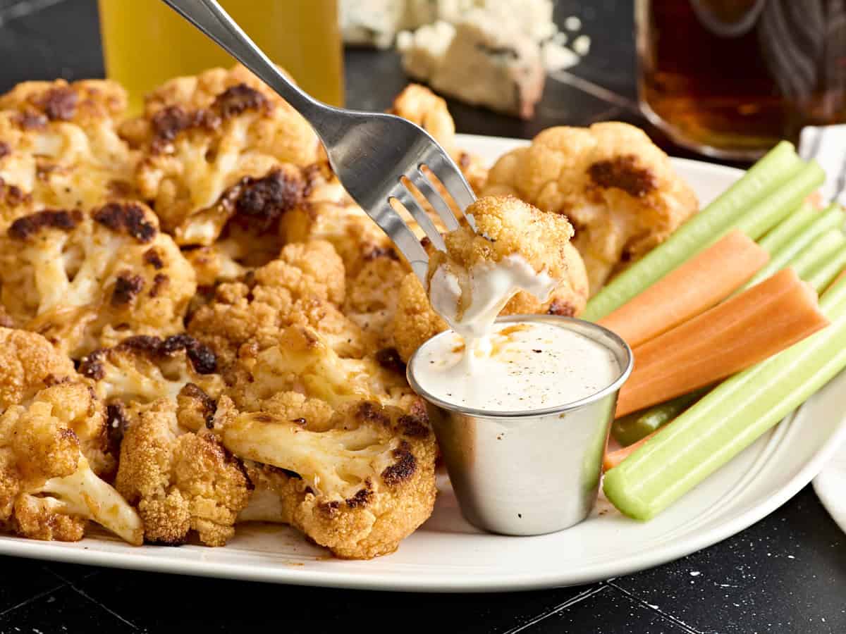 Side view of buffalo cauliflower wings on a plate, with one being dipped into ranch dressing by a fork.