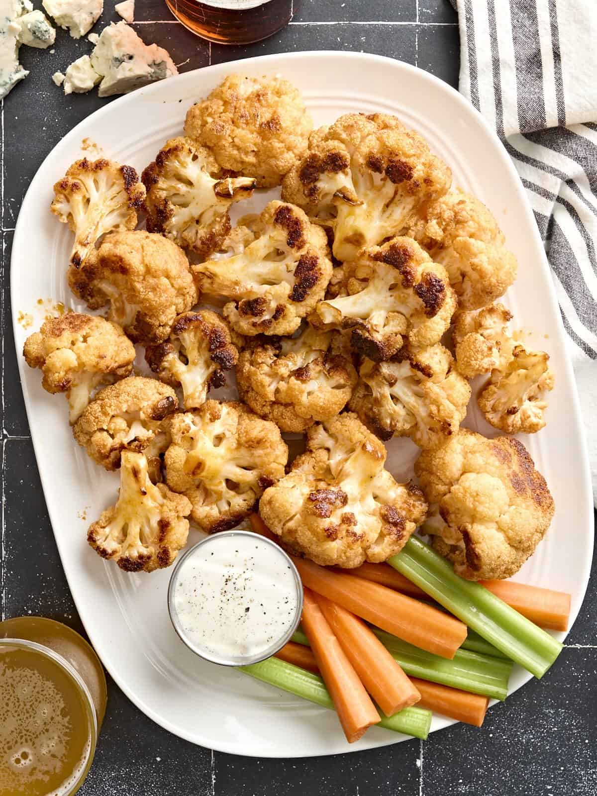 Overhead view of buffalo cauliflower wings on a plate with celery sticks, carrot sticks, and dip.