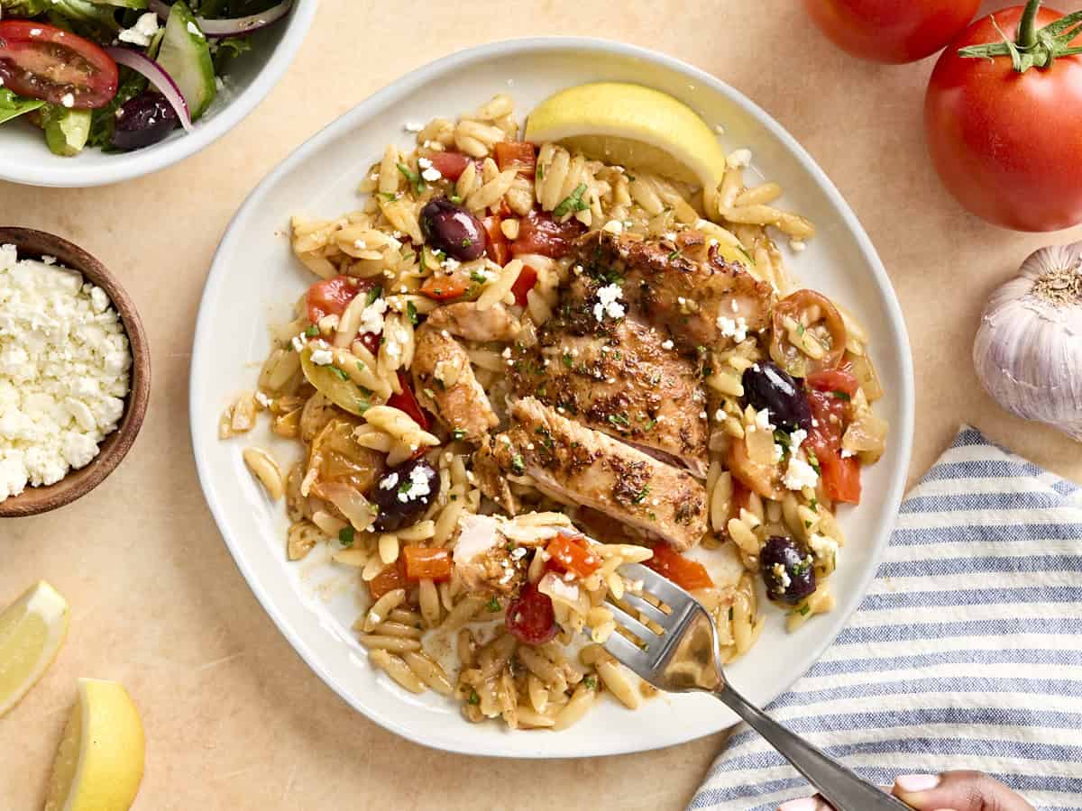 A fork taking some orzo from a plate with Greek chicken.