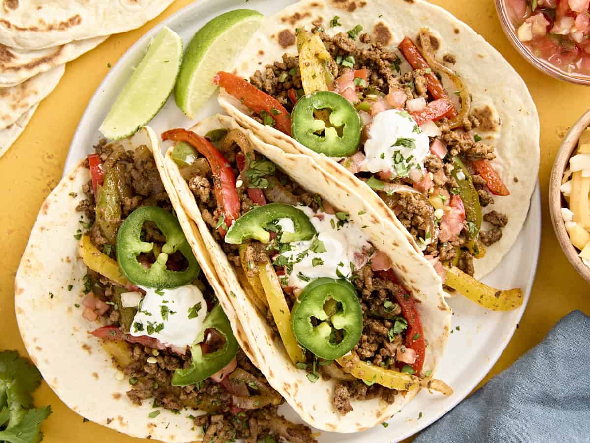 Overhead view of ground beef fajitas on a plate, topped with sour cream and jalapeno slices.