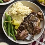 Overhead view of mississippi pot roast on a plate with mashed potatoes and green beans, with a fork taking some of the meat.