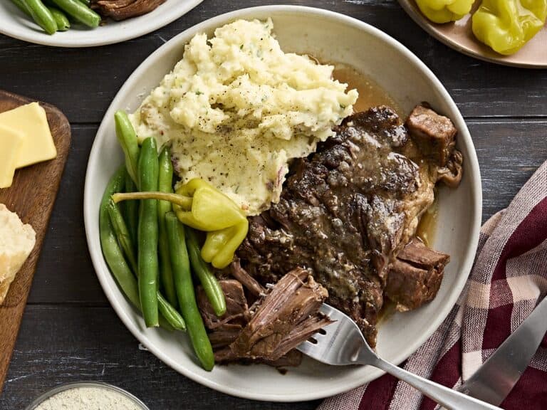 Overhead view of mississippi pot roast on a plate with mashed potatoes and green beans, with a fork taking some of the meat.