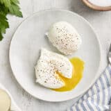 Overhead view of two poached eggs on a plate, with one cut open and the yolk running from it.