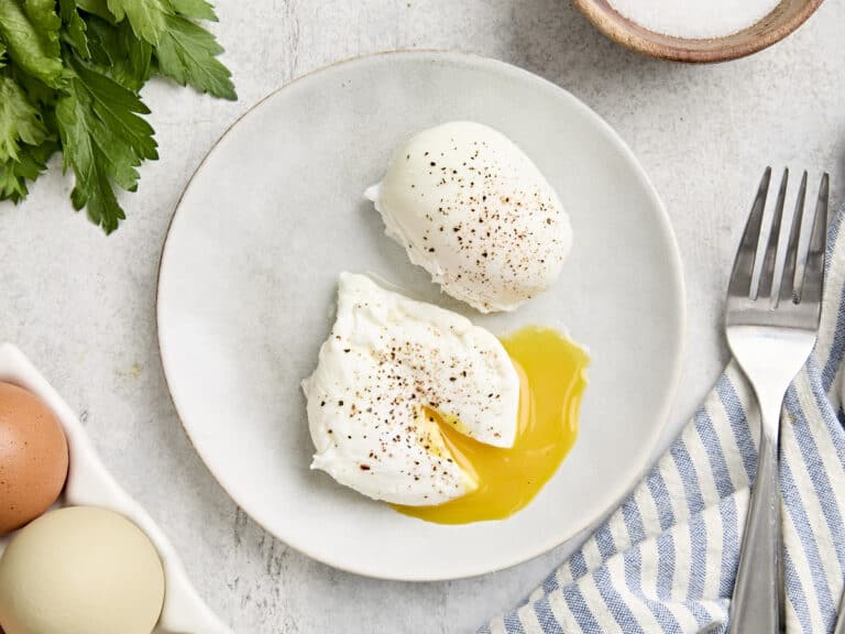 Overhead view of two poached eggs on a plate, with one cut open and the yolk running from it.