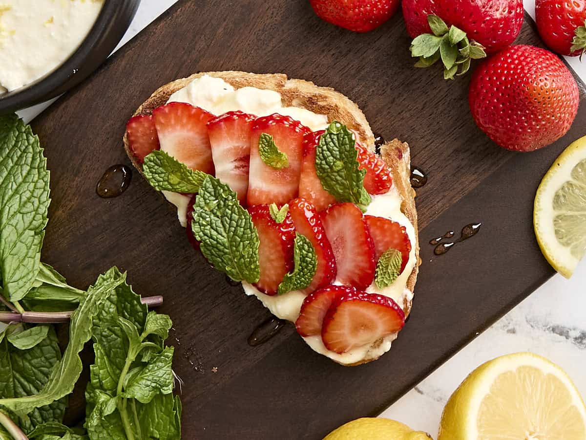 Overhead view of ricotta toast with sliced strawberries, mint, and honey.