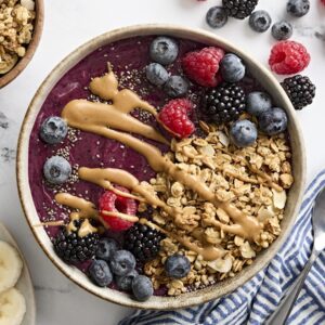 Overhead view of a smoothie bowl topped with granola, chia seeds, berries, and peanut butter.