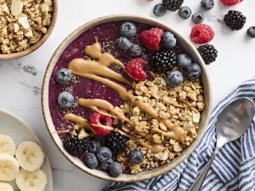 Overhead view of a smoothie bowl topped with granola, chia seeds, berries, and peanut butter.