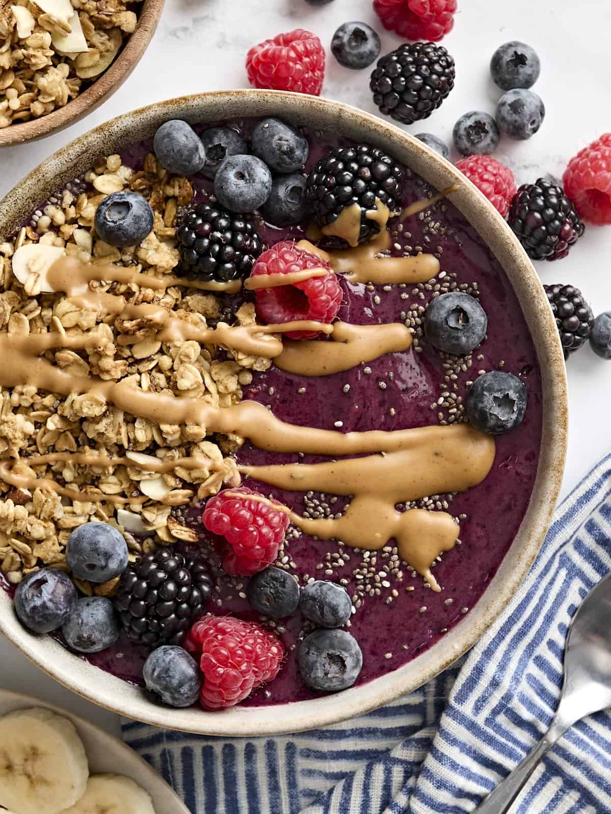 Overhead view of a smoothie bowl topped with granola, chia seeds, berries, and peanut butter.