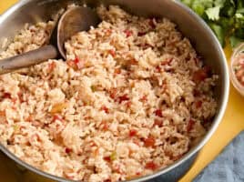 Side view of spanish rice in a skillet with a wooden spoon.