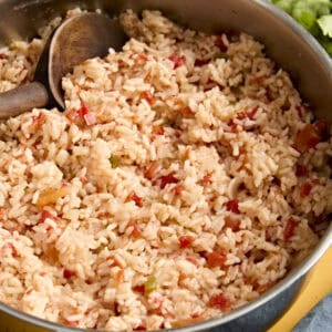 Side view of spanish rice in a skillet with a wooden spoon.