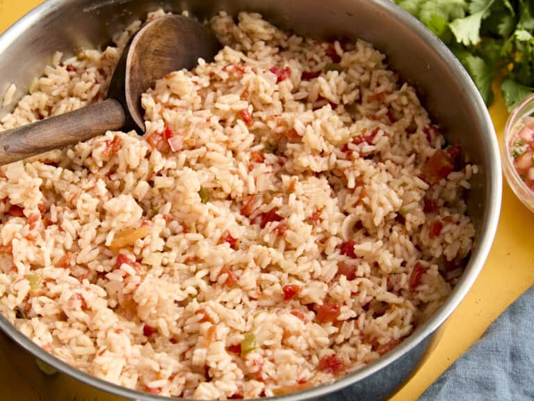 Side view of spanish rice in a skillet with a wooden spoon.